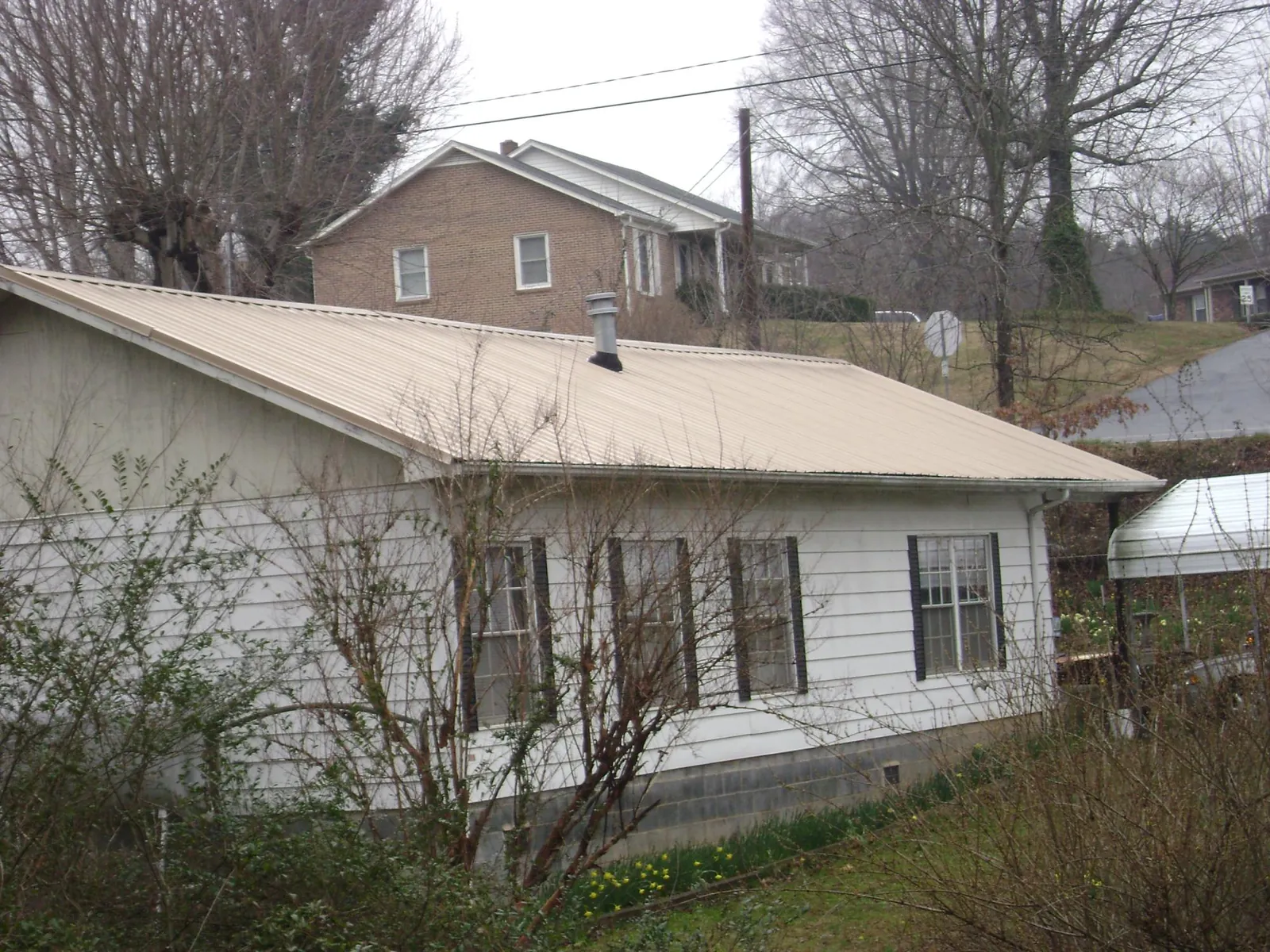 Tan metal roof on a white sided house set into a hillside — Commercial Roofing by Roofing Brothers in Middlesex